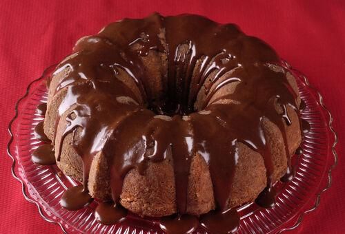 a bundt cake with chocolate icing sitting on a glass plate next to a red cloth