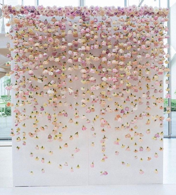 a white wall with pink and yellow flowers hanging from it's sides in front of a large window