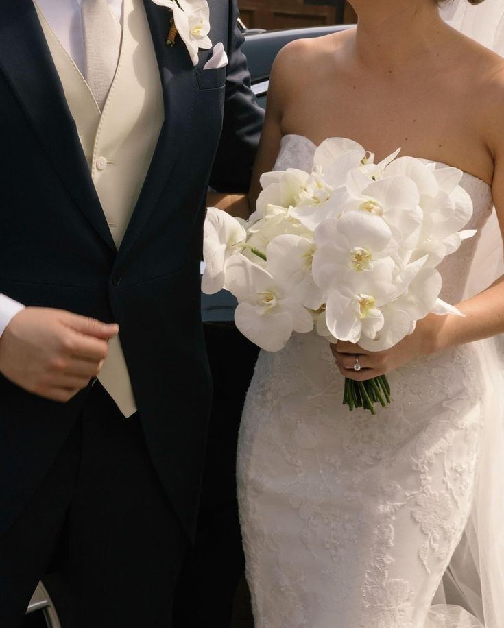 the bride and groom are standing together in their wedding day attire, holding white flowers