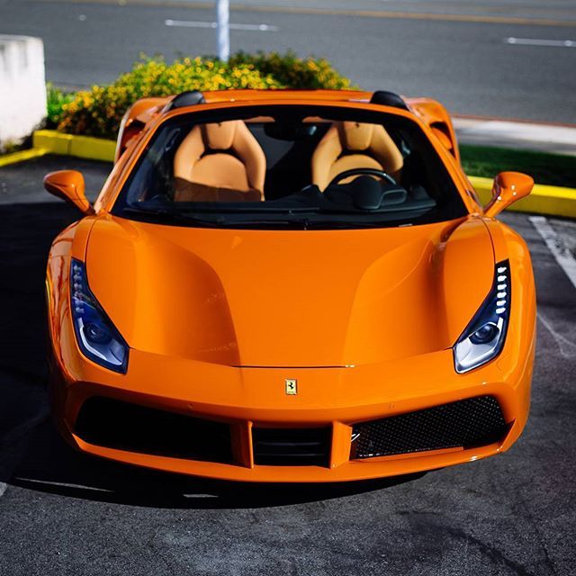 an orange sports car parked in a parking lot with its doors open and two people inside