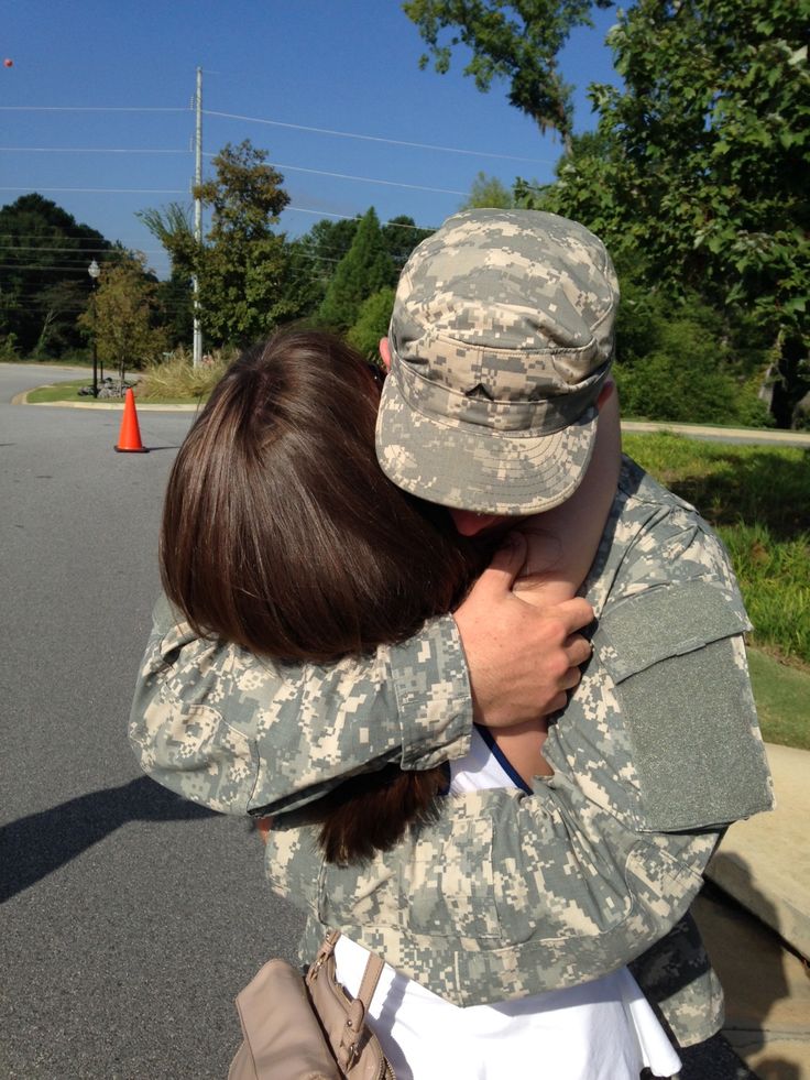 a soldier hugging a woman in the middle of the street with trees in the background