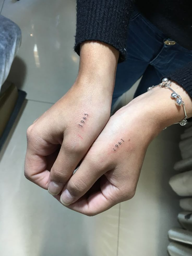 two people holding hands with the word love tattooed on their fingers, both wearing matching bracelets