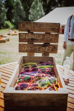 a wooden box filled with lots of different colored glasses next to a sign that says don't be blinded by our love