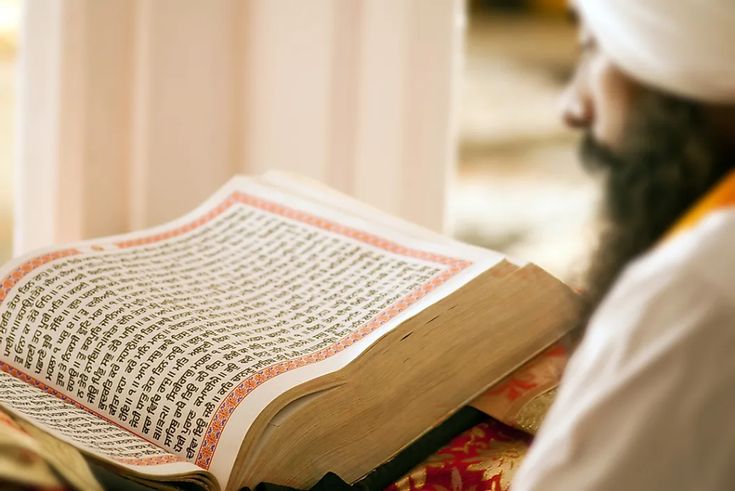 a man reading the koran while wearing a white turban and holding an open book