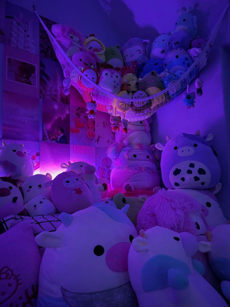 a room filled with lots of stuffed animals on top of a purple bed sheet covered in pink and blue lights