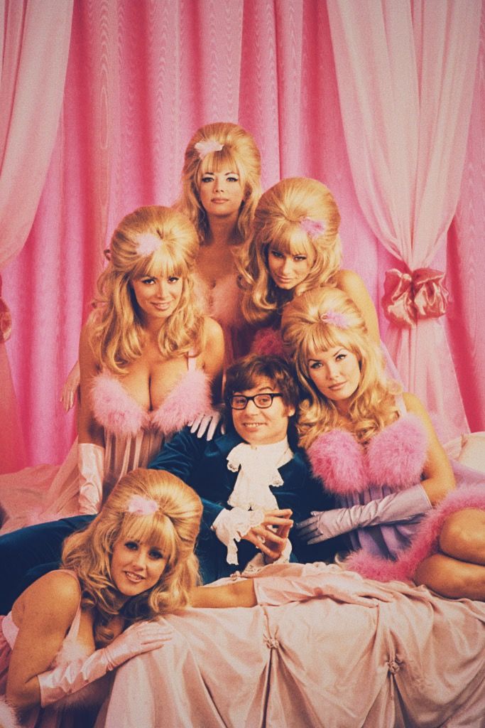 a group of women sitting on top of a bed in front of pink drapes