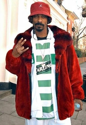 a man in a red jacket and hat standing on the sidewalk with his hand up