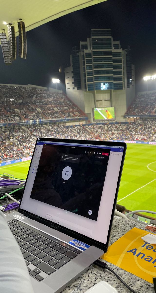 an open laptop computer sitting on top of a table in front of a soccer field