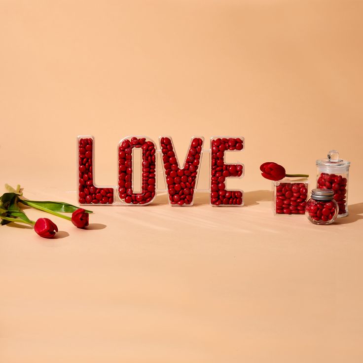 the word love spelled out with red beads and rose petals next to it is surrounded by flowers