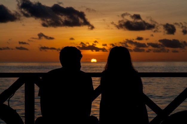 two people sitting on a bench watching the sun go down over the ocean in silhouette