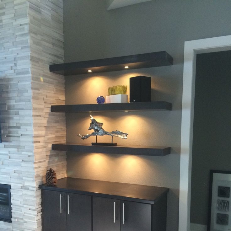 a living room with some shelves and lights on the wall next to a fire place