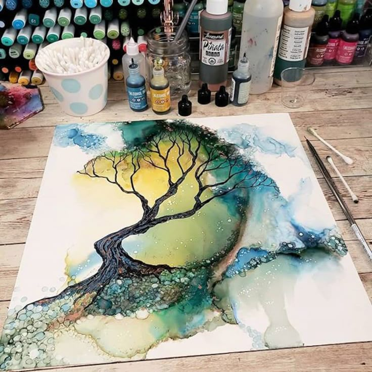 a painting is being made with alcohol bottles and paintbrushes on the table next to it