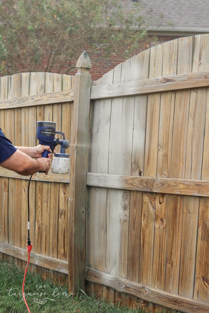 a man using a paint sprayer on a wooden fence next to a yard with grass