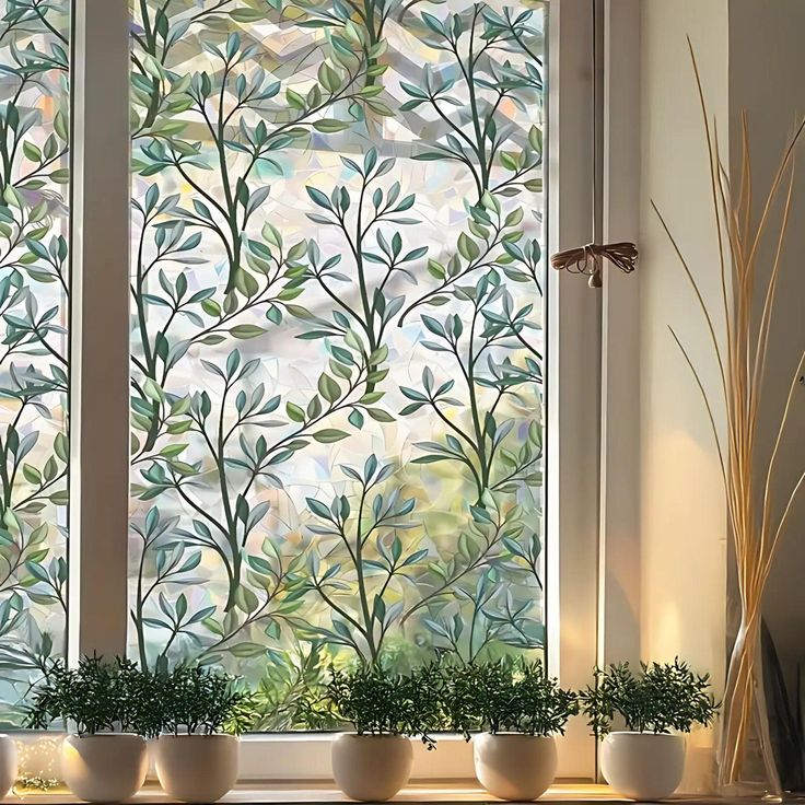 three planters sit in front of a window with leaves drawn on the glass behind them