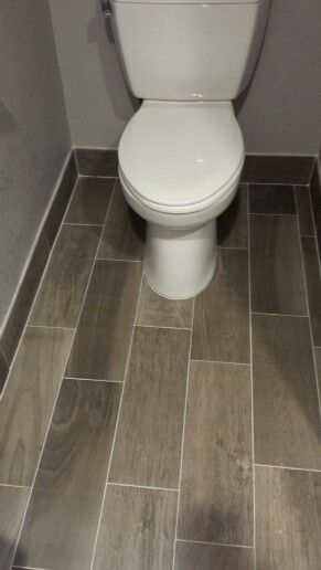 a white toilet sitting inside of a bathroom next to a tiled floor with gray walls