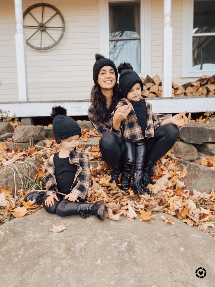 a woman and two children sitting on leaves in front of a house