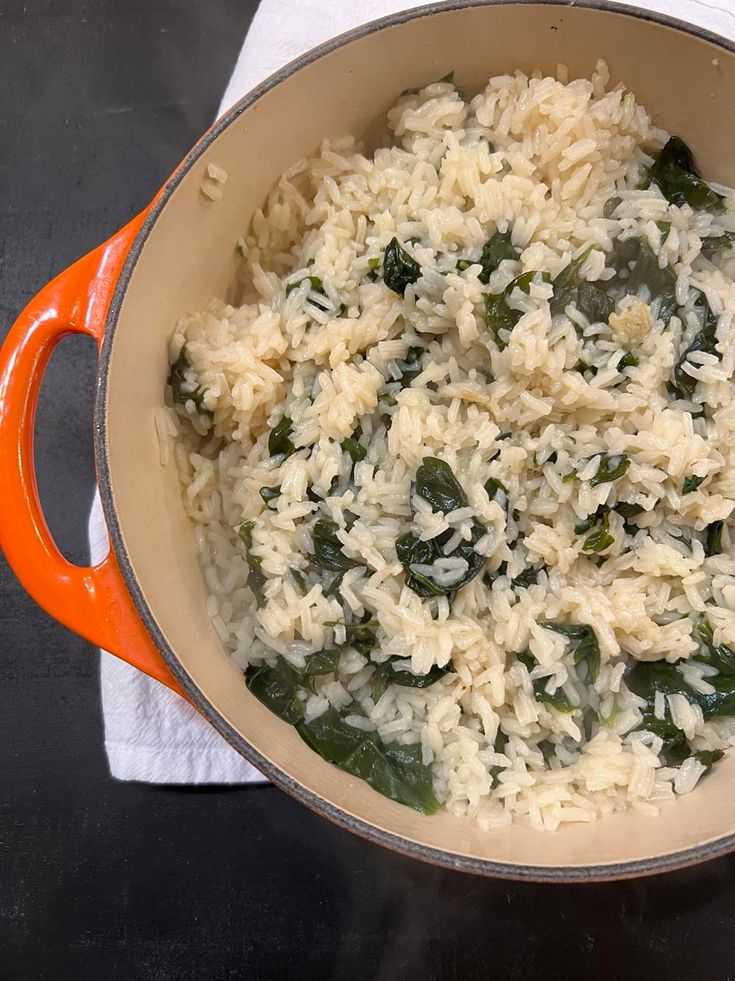 a pot filled with rice and spinach sitting on top of a table next to a napkin