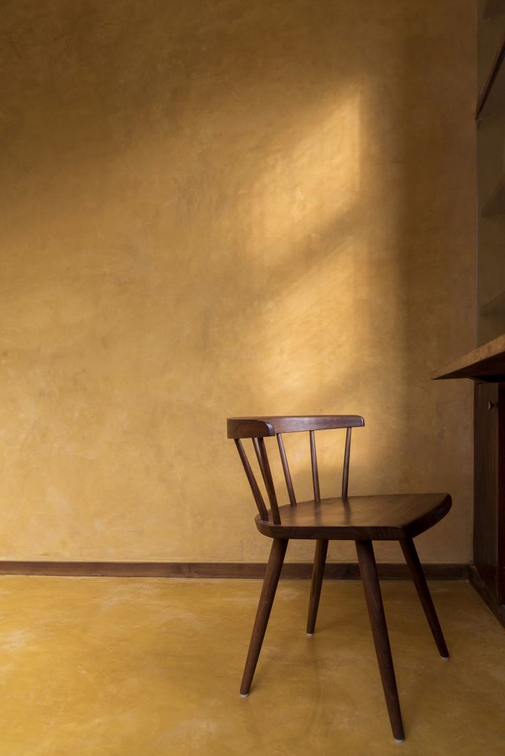 a wooden chair sitting in front of a yellow wall