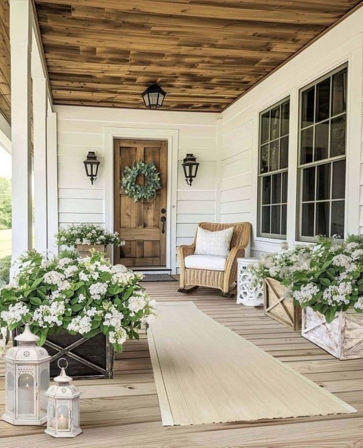 the front porch is decorated with white flowers and potted plants