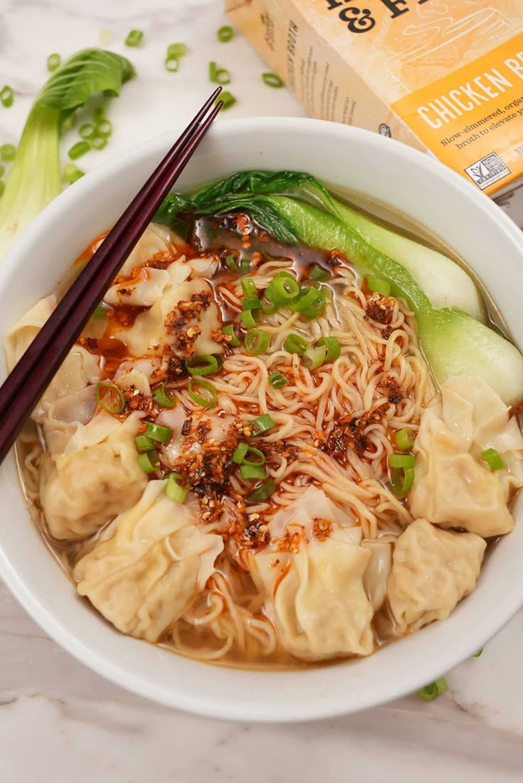 a white bowl filled with noodles and vegetables next to chopsticks on a table