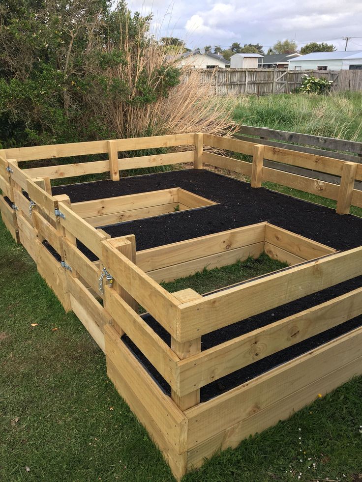 a wooden raised garden bed with black soil in the middle and green grass around it