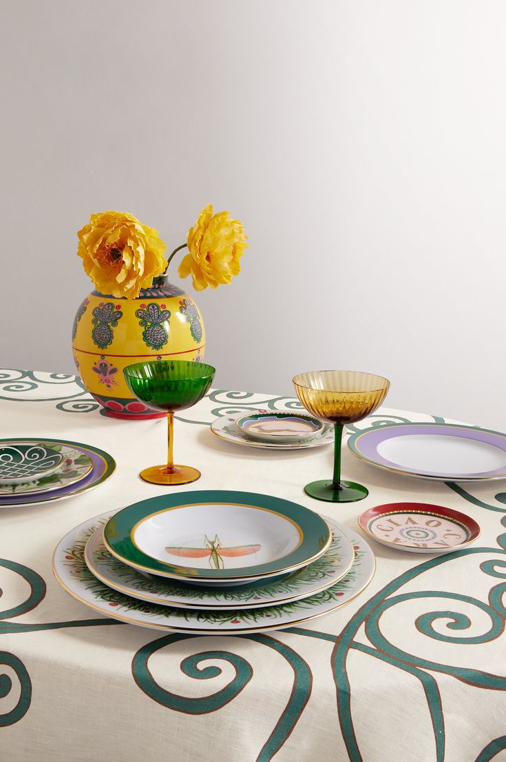 a table topped with plates and vases filled with yellow flowers next to each other