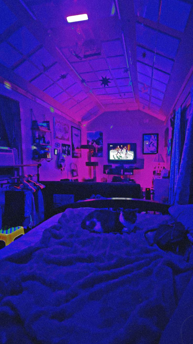 a bed in a room with purple lights on the ceiling and a television set behind it