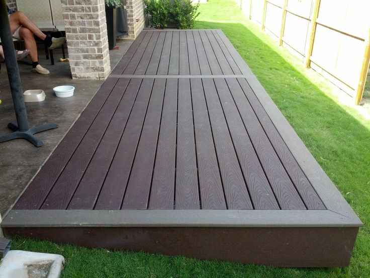 a person sitting on a bench next to a wooden deck in the grass near a brick building