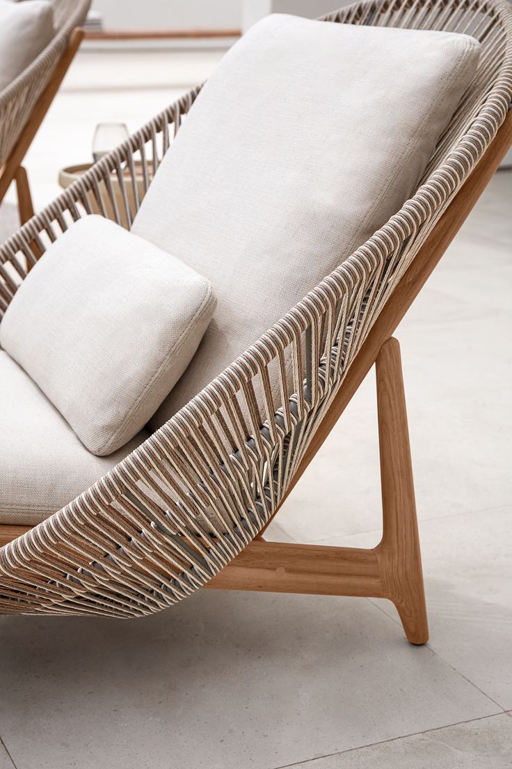 two wicker lounge chairs with white pillows on top of each one, sitting side by side