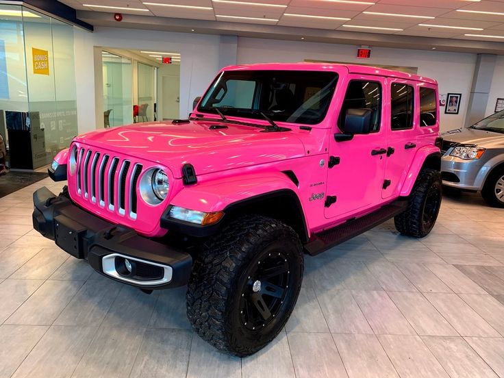 a bright pink jeep is parked in a showroom with two other cars behind it