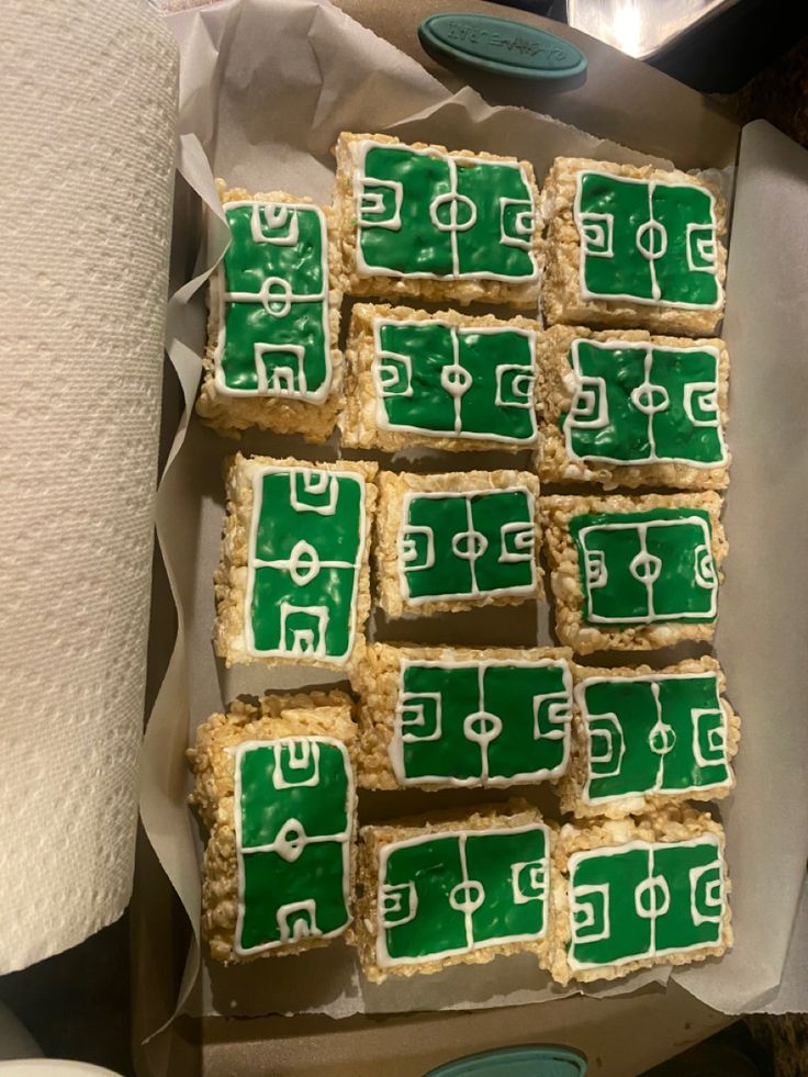 several green and white decorated cookies in a box with paper towels next to them on a table