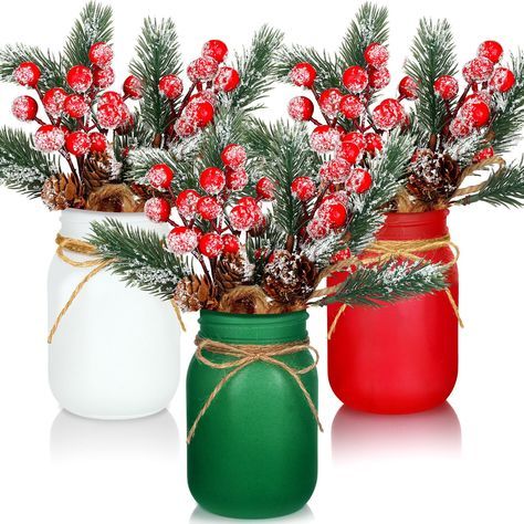 two mason jars filled with red and white berries next to pine cones on top of each other