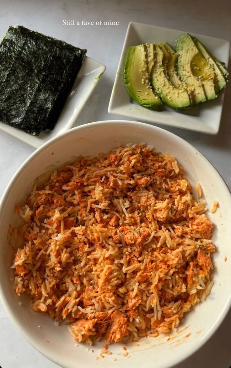 a white bowl filled with shredded carrots next to sliced avocado and sushi