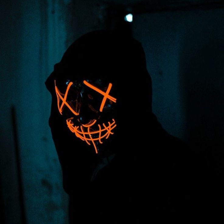 a man wearing a neon mask with the cross on it's face in a dark room