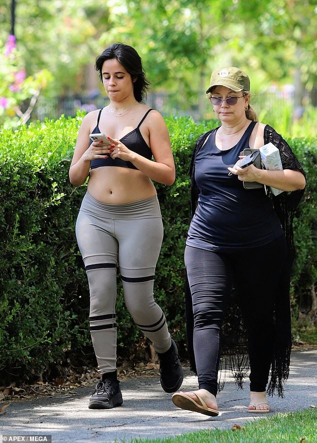 two women are walking down the sidewalk while looking at their cell phones and one is wearing leggings