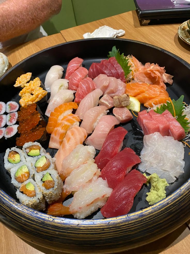 a black bowl filled with lots of different types of sushi on top of a wooden table