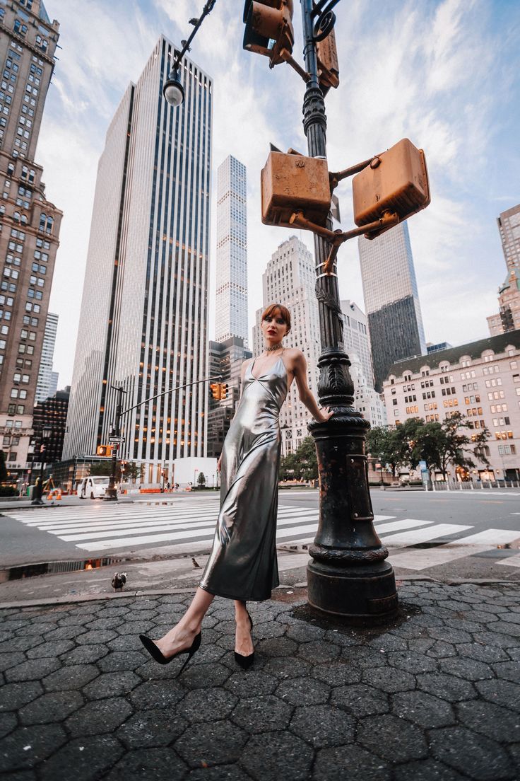 a woman standing next to a street light in front of tall buildings and skyscrapers