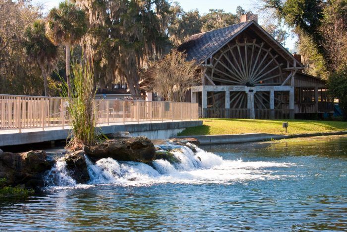 a river running under a bridge next to a wooden building with a water wheel on it