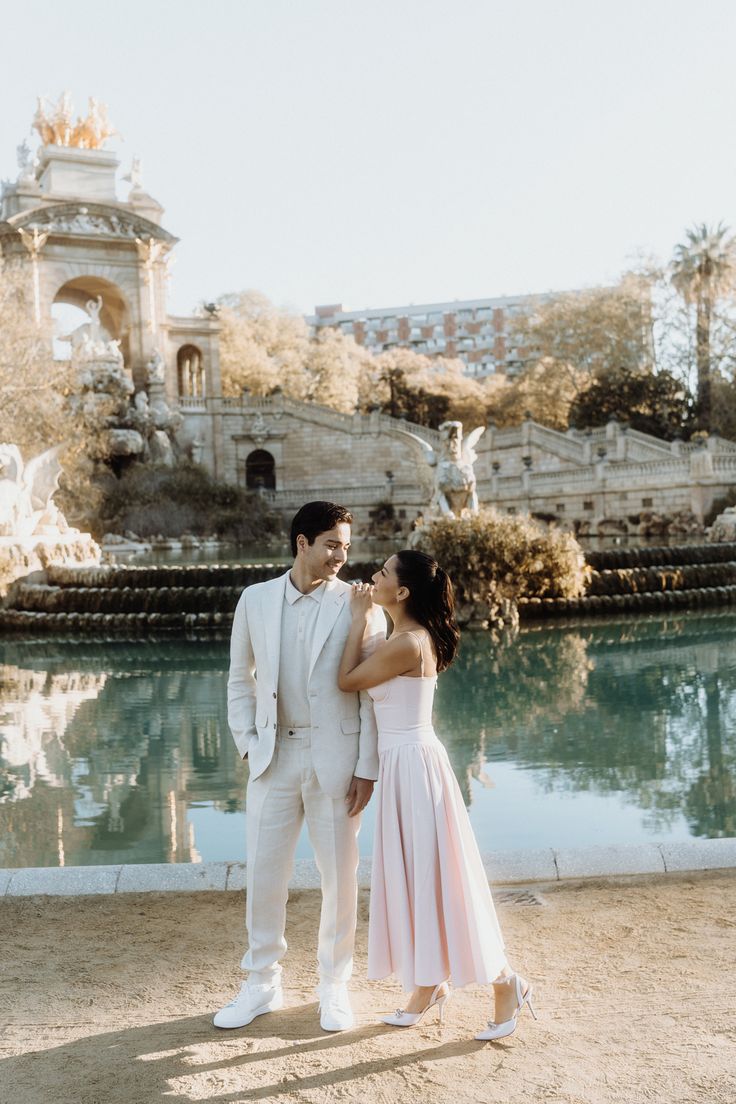 a man and woman standing next to each other in front of a pond with fountains