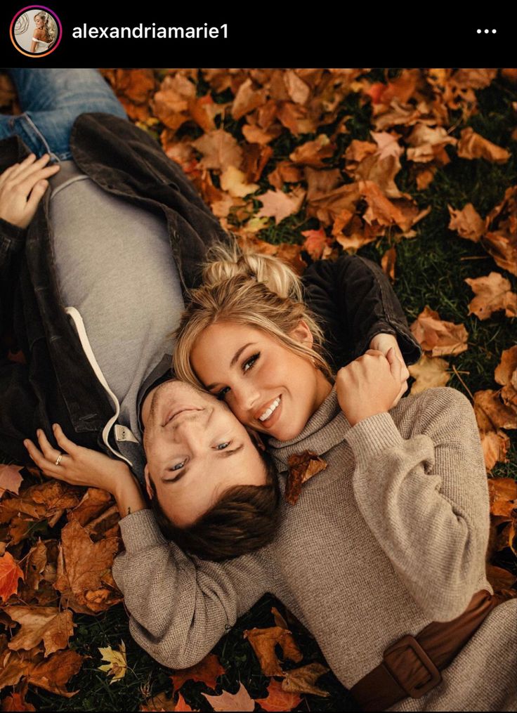 two people laying on the ground surrounded by leaves and looking at the camera with love