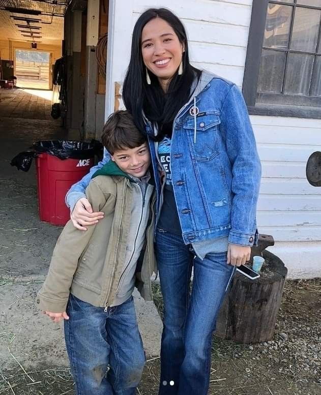 a woman standing next to a boy in front of a white building with a blue jacket on