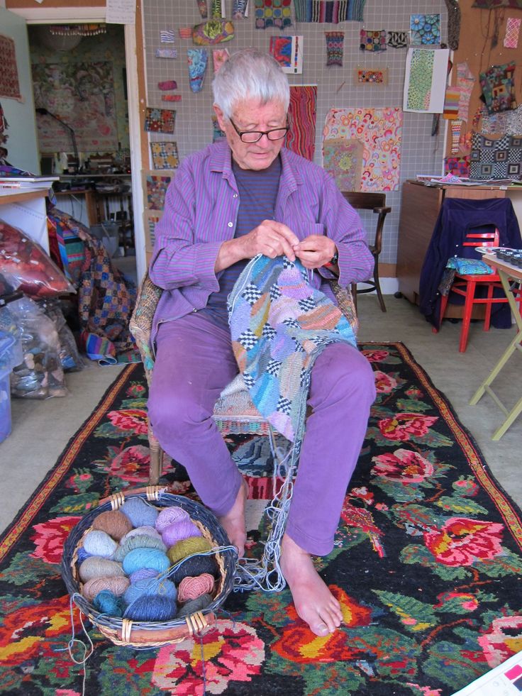 an older woman sitting on a chair in front of a pile of balls of yarn