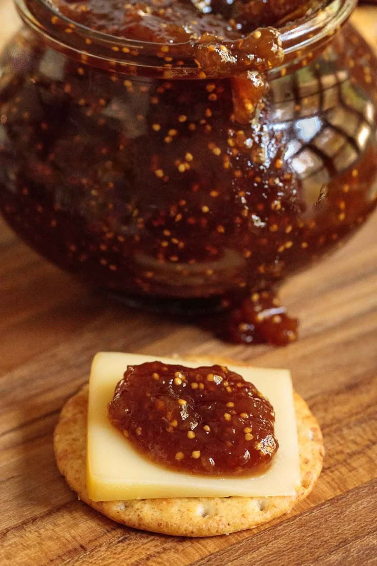 a cracker with jam and cheese on it next to a jar filled with jelly