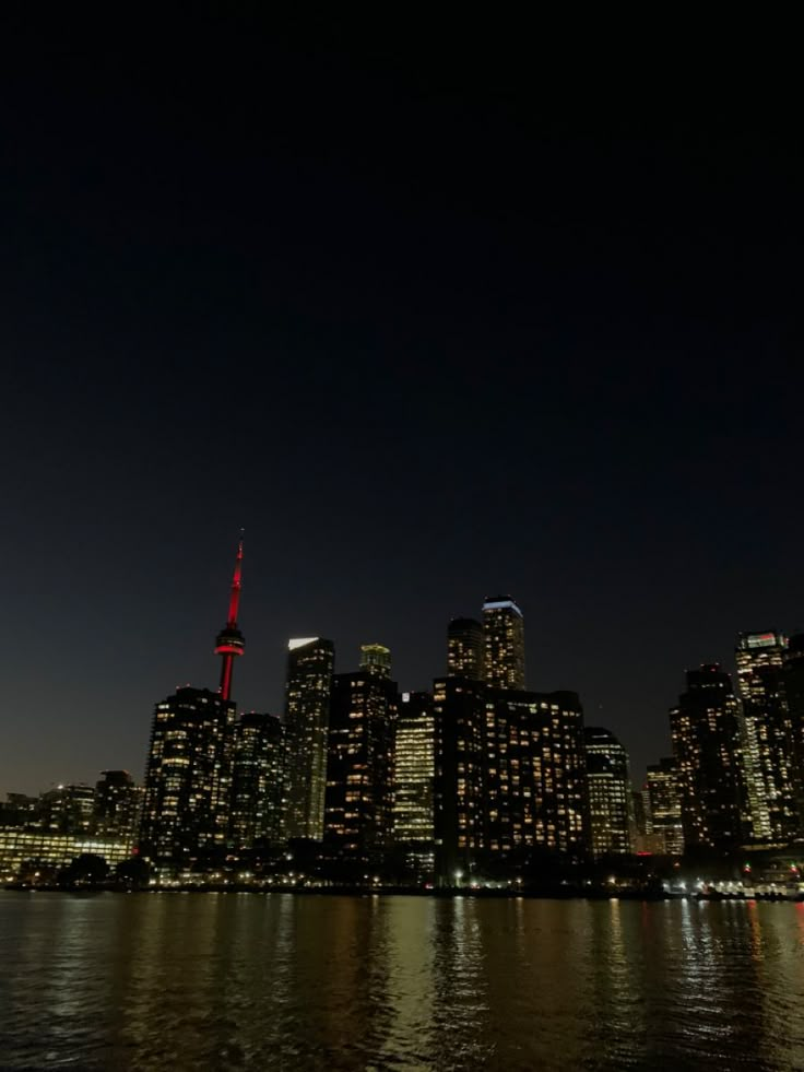 the city skyline is lit up at night, with bright lights reflecting in the water