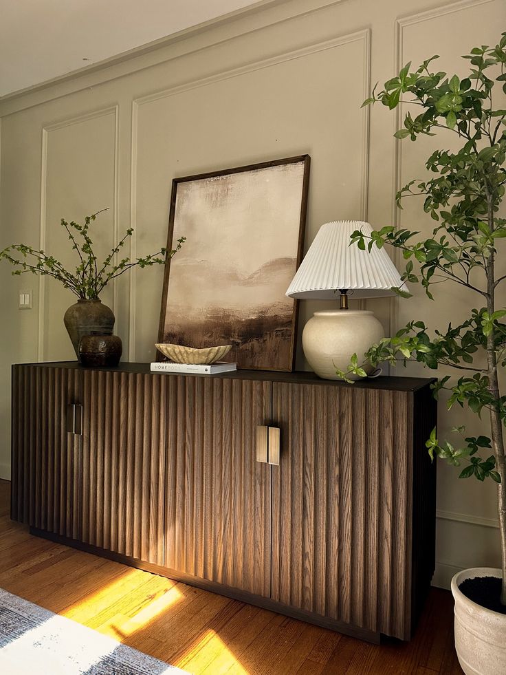 a living room with a plant on top of a wooden cabinet next to a lamp