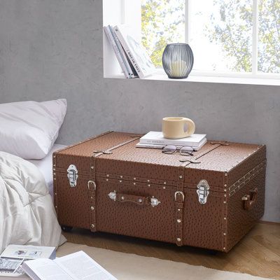 a brown suitcase sitting on top of a bed next to a window