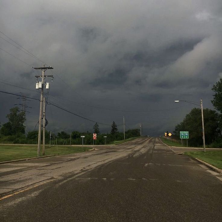 an empty road with storm clouds in the distance and street signs on either side,