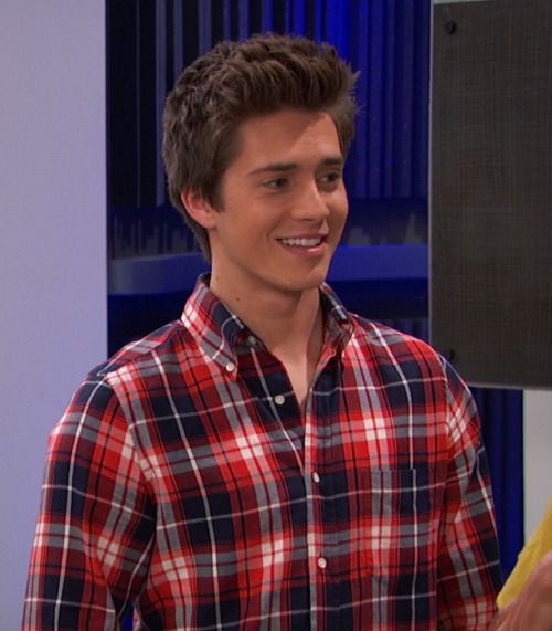 the young man is wearing a red and black plaid shirt while talking to someone in front of him