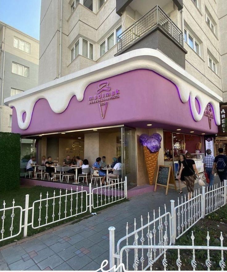 an ice cream shop with purple icing on the front and white fence around it