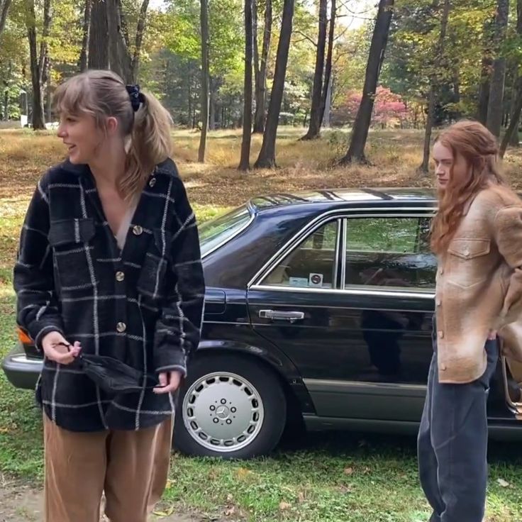 two women standing in front of a car talking to each other on the side of the road